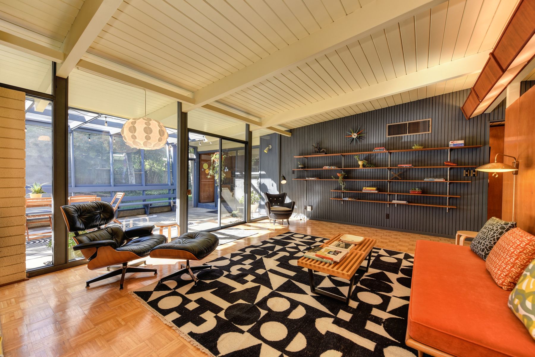 A finished living room: a timber-lined ceiling, walnut shelving and full-height glazing opening onto the garden.
